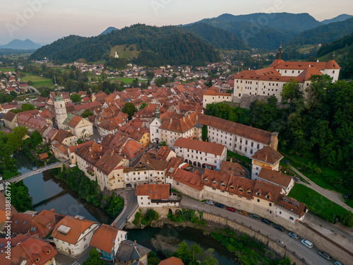 Obraz na płótnie Beautiful Skofja Loka medieval town with church and the castle at sunset. Aerial view of riverfront with historic houses and the bridges over Sora river. Hilly landscape towards Smarna Gora. w salonie