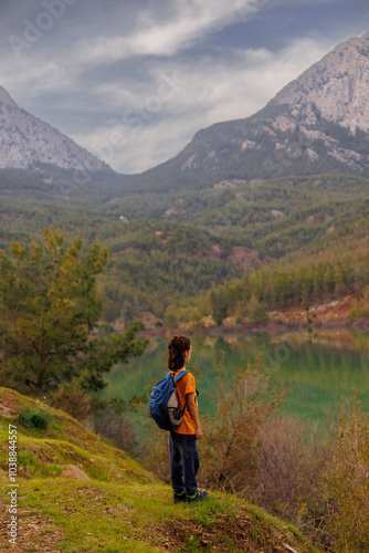 summer camp. a boy with a backpack looks at a beautiful mountain lake. Relaxed, peaceful, thoughtful, happy and free child on a mountain lake.