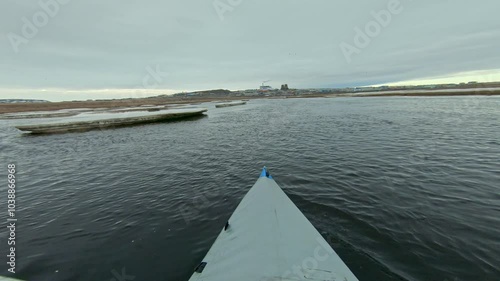 First-person view kayak paddling on a river with ice floes. Spring melting ice on a river in the suburbs. The skyline and industrial buildings in the distance.