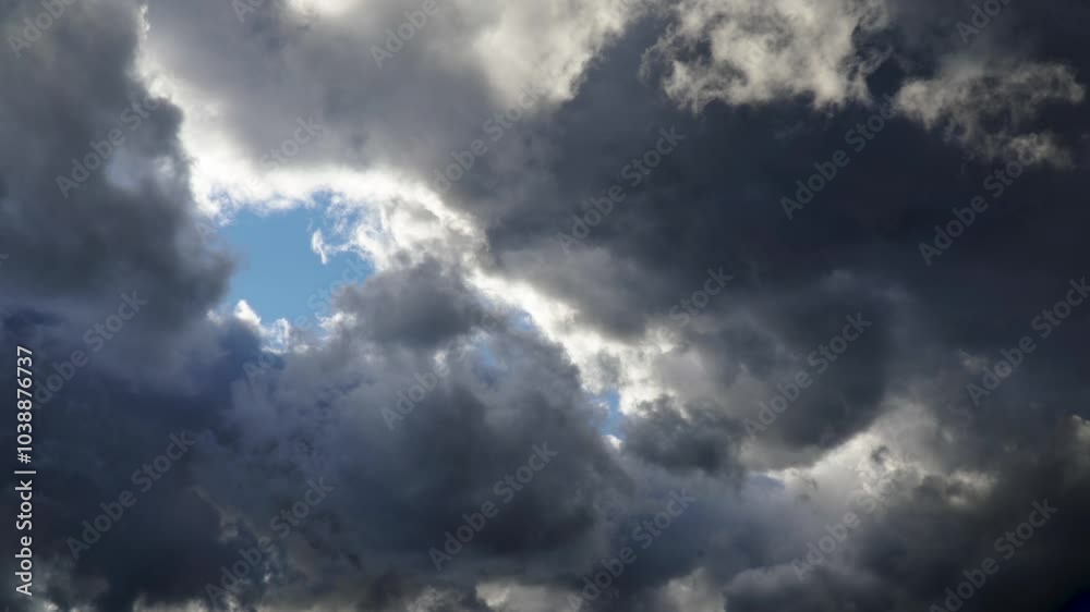 An intense view of dark storm clouds, with a small patch of blue sky peeking through. The interplay of light and shadow creates a moody atmosphere, emphasizing the power and drama of nature An intense view of dark storm clouds, with a small patch of blue sky peeking through. The interplay of light and shadow creates a moody atmosphere, emphasizing the power and drama of nature