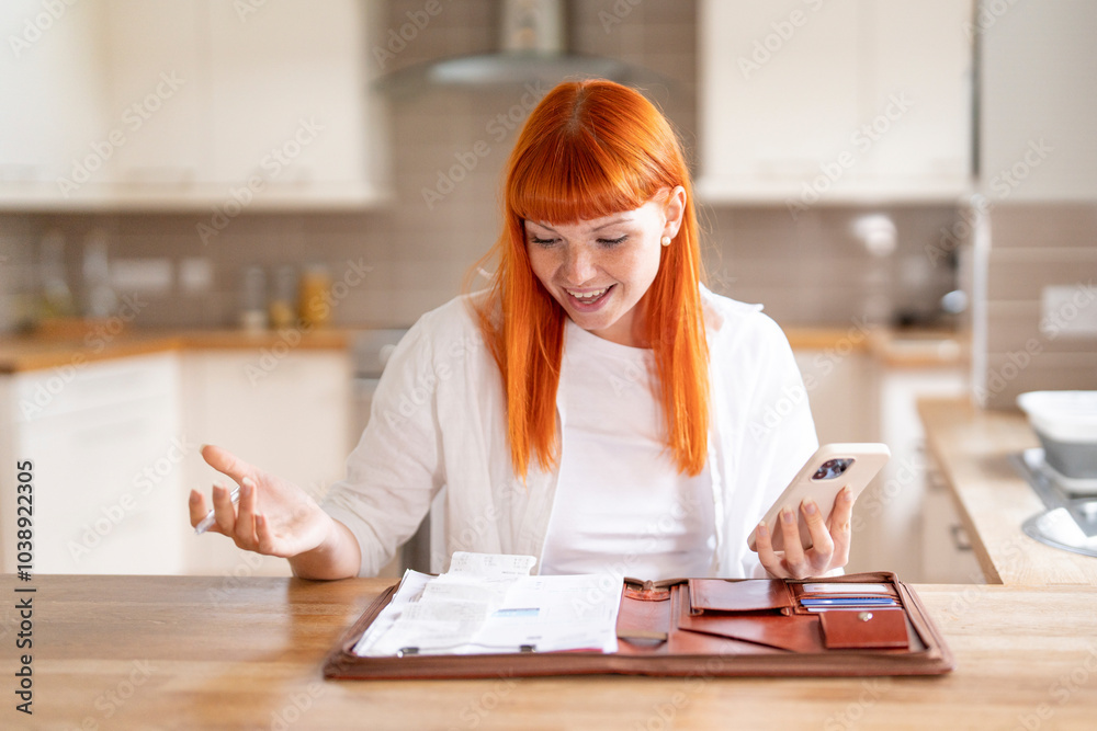 A delighted woman reviews her budget and bills while sitting at a cozy kitchen table with a smartphone in hand A delighted woman reviews her budget and bills while sitting at a cozy kitchen table with a smartphone in hand
