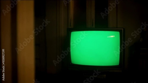 tv with a green screen on the screen, dimli lit room