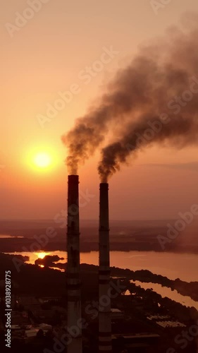 Dangerous fumes from industry pollute the air. Harmful factory with smoking pipes near river at sunset. Global warming. Environmental pollution. Vertical video