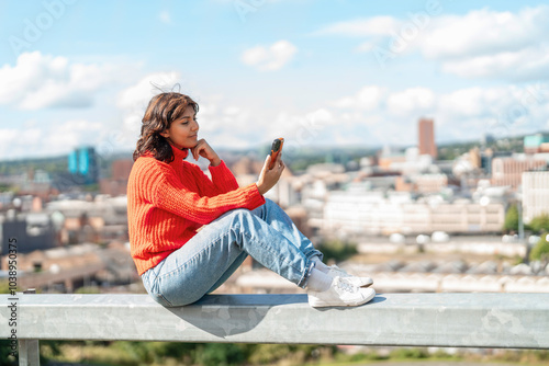 Εκτύπωση καμβά Young woman enjoying a sunny day while sitting on a rooftop ledge and using her