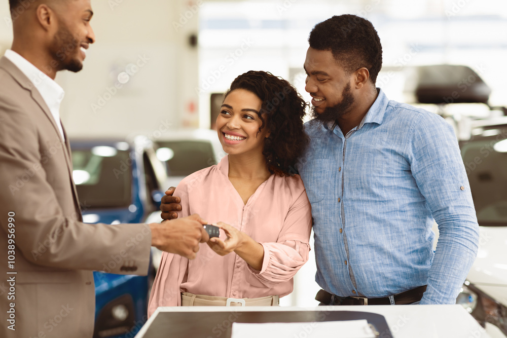 Dealer Giving New Car Key To Joyful Black Buyers Couple Standing In Auto Dealership Store. Family Buying Automobile. Selective Focus Dealer Giving New Car Key To Joyful Black Buyers Couple Standing In Auto Dealership Store. Family Buying Automobile. Selective Focus
