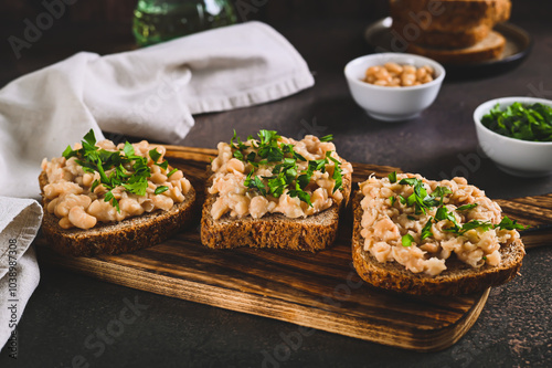 Appetizing sandwiches on grain bread with mashed beans and greens on a board on a table