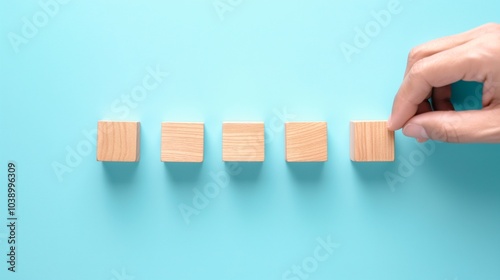 A hand adjusts one of five wooden blocks on a light blue surface during a creative activity or brainstorming session photo