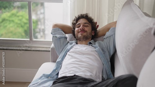 Happy lazy young man relax daydream meditate sit on comfortable sofa at home in living room, calm guy rest breathing fresh air having nap with eyes closed feel peace of mind, no stress free relief
