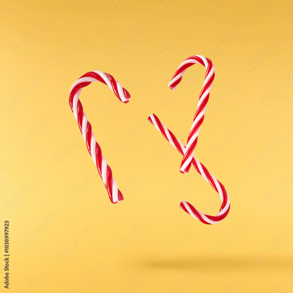 Obraz premium Christmas holliday image, Christmas bauble in shape of a christmas stick lolipop falling in the air isolated on yellow background