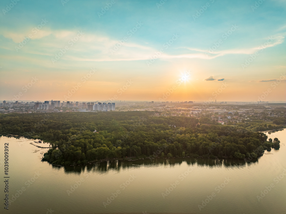 Obraz premium Big lake with green shores in bright sun light and city on horizon, aerial landscape. Recreation concept. Aerial view