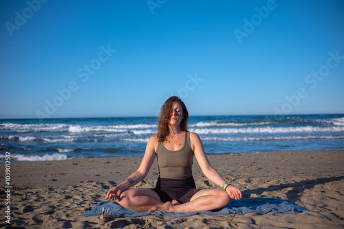 Girl in sportswear doing yoga on sea sand beach. Morning yoga on seashore under clear blue sky. Sporty young woman maintains healthy lifestyle