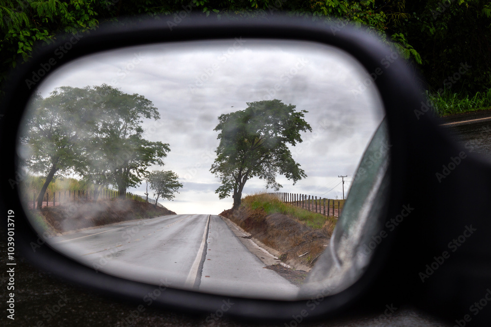 Detalhe de um retrovisor, molhado de chuva, refletindo a paisagem do local. Detalhe de um retrovisor, molhado de chuva, refletindo a paisagem do local.