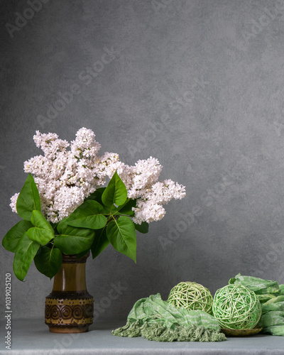 Bouquet of lush white lilacs in dark vase on gray background. Small white flowers contrast with green leaves and stand out on dark vase, giving still life an elegant look. Copy space.