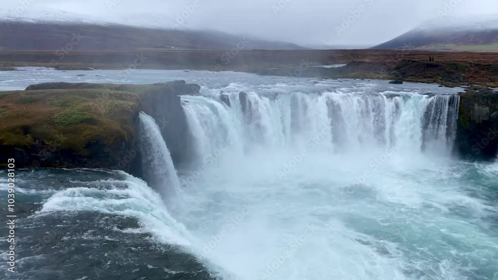 Godafoss waterfall flowing in Iceland under a cloudy sky, with tourists admiring the stunning natural feature and capturing the beauty of the landscape Godafoss waterfall flowing in Iceland under a cloudy sky, with tourists admiring the stunning natural feature and capturing the beauty of the landscape