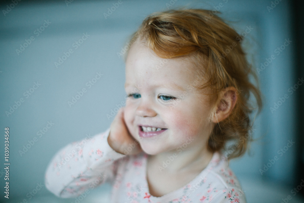 Aesthetic minimalistic Portrait of a cute happy ginger-haired blue-eyed baby girl in pyjamas after her nap
