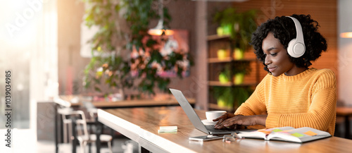 Young afro woman having online training, using laptop and wireless headset at cafe, free space photo