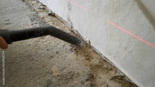 Construction worker vacuuming dust on concrete floor.