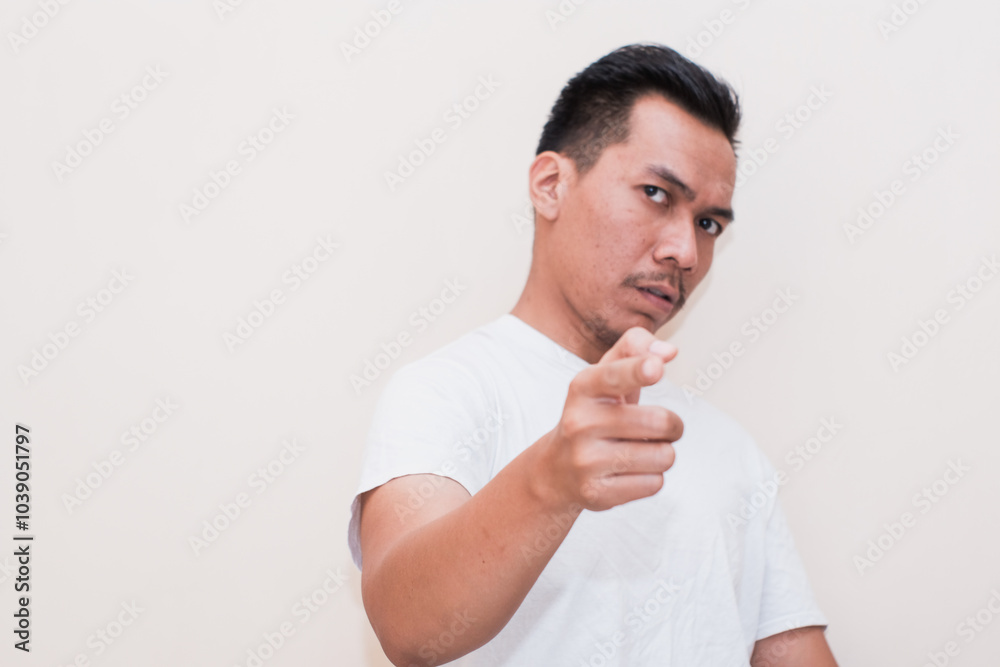 Very angry aggressive Southeas Asian man portrait in white t-shirt pointing to camera on isolated white background. Very angry aggressive Southeas Asian man portrait in white t-shirt pointing to camera on isolated white background.