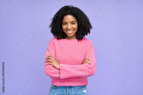 Smiling ethnic Afro American female fashion model looking at camera. Portrait of young happy curly pretty cool gen z African woman wearing pink sweater standing isolated on purple background.