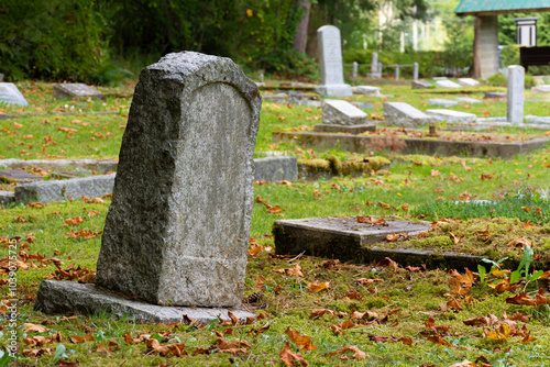An image of an old weathered gravesite marker which is leaning to one side. 