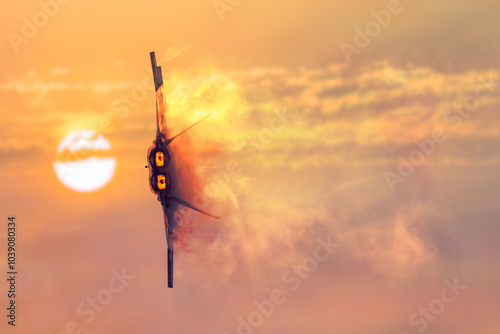 Fotografie A military jet on its side fires the engines leaving a vapor trail in its wake