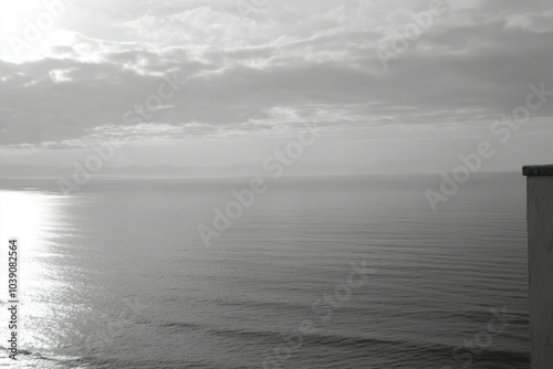 A Grayscale View of a Calm Sea with a Cloudy Sky and a Partial Wall on the Right