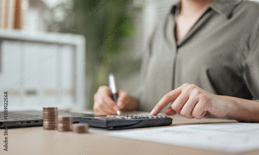Fototapeta premium financial, analyzing, finance, wealth, investment, analysis, growth, calculate, planning, profit. A woman is writing on a calculator with a pen. She is surrounded by coins and a stack of papers.