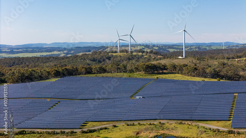 Aerial drone view of a hybrid solar and wind farm showing the large wind turbines in the background for renewable clean energy supply located at Bannister, NSW, Australia on a sunny day