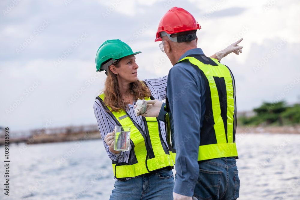 Environmental scientists or workers, wearing safety helmets and gloves, examining waste materials along a shoreline are large industrial tanks environmental waste water or pollution effects concept. Environmental scientists or workers, wearing safety helmets and gloves, examining waste materials along a shoreline are large industrial tanks environmental waste water or pollution effects concept.