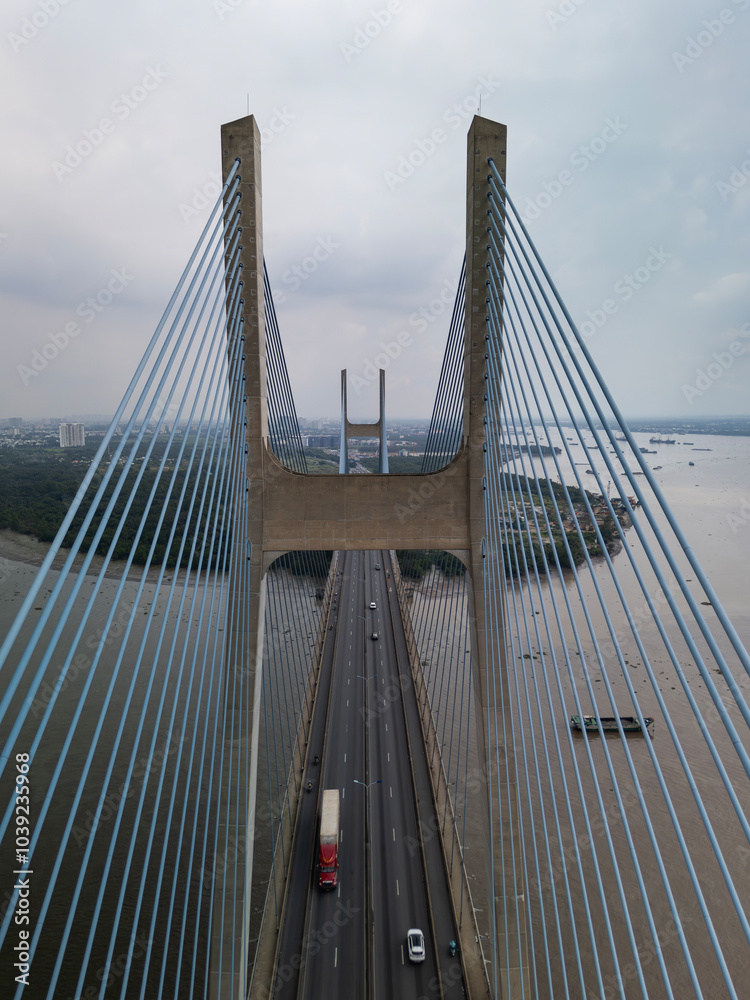 Obraz premium View of Phu My Bridge in Ho Chi Minh City Vietnam during the day. Symmetrical view directly along the traffic lanes and cables with shipping under bridge in vertical format. 