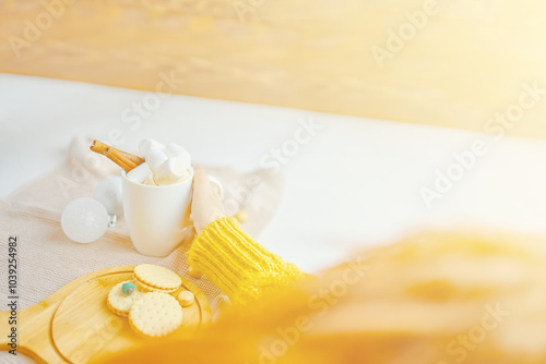 Person enjoying hot drink with whipped cream and biscuits in cozy, sunny spot, creating cozy atmosphere