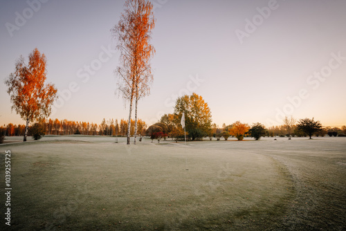 A frosty golf course at sunrise with birch trees and autumn foliage, capturing the peaceful, serene beauty of the early morning landscape.. photo