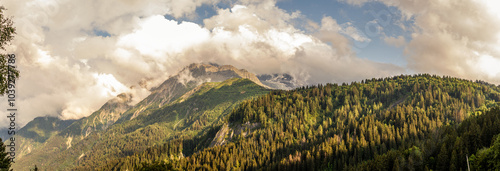 Tops of Alps mountains in clouds with sky, green forest on the france normal way to top of Mont Blanc photo