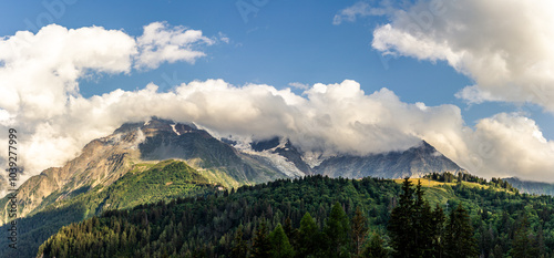 Tops of Alps mountains in clouds with sky, green forest on the france normal way to top of Mont Blanc photo