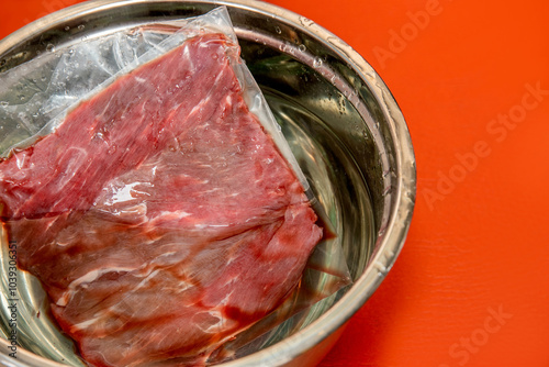 Piece of raw meat defrosting in a bowl on red background. defrosting, frozen