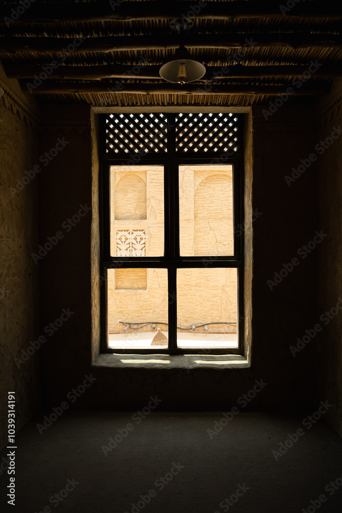 View through traditional window from dark interior, looking out to sunlit beige walls with arches and decorative carvings. Contrast between light and shadow. Old dirty wooden window View from inside View through traditional window from dark interior, looking out to sunlit beige walls with arches and decorative carvings. Contrast between light and shadow. Old dirty wooden window View from inside