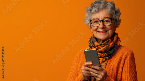 Senior woman holding a smartphone against an orange background