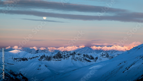 sunrise on queyras mountain range in winter; shadows of mountains with the morning sun; view on snowy mountains with moon in the sky photo