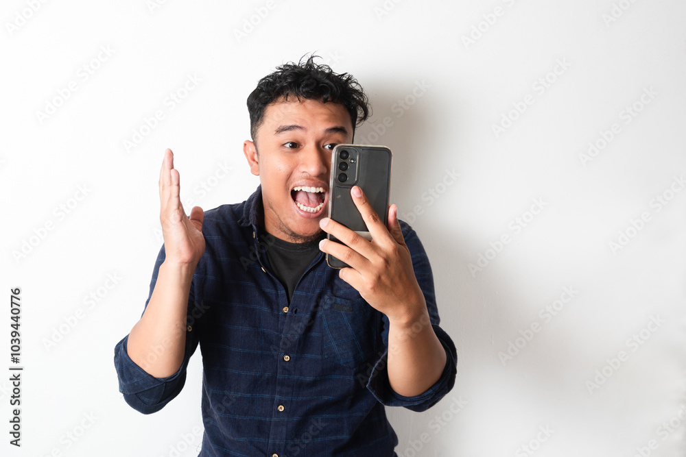 Adult Asian man showing happy face expression while looking to the mobile phone screen Adult Asian man showing happy face expression while looking to the mobile phone screen