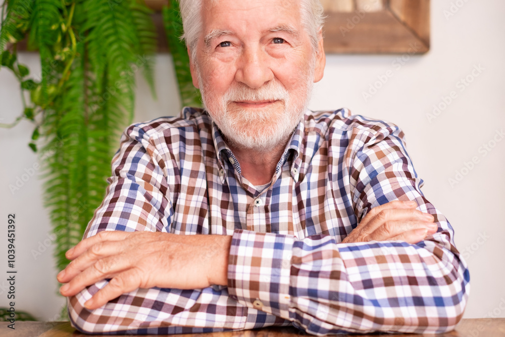 Portrait of handsome smiling bearded senior man with crossed arms sitting at cafe table. Elderly caucasian male wearing checkered shirt Portrait of handsome smiling bearded senior man with crossed arms sitting at cafe table. Elderly caucasian male wearing checkered shirt