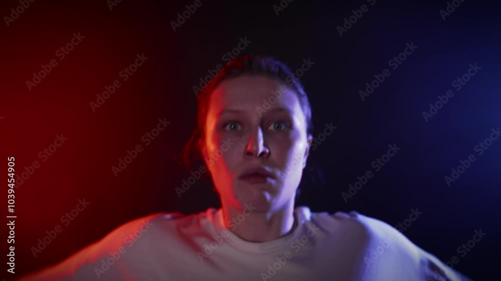 Shocked woman looking at camera and dancing in dark studio, red and blue light. Emotions and feelings of young adult female dancer moving in dancehall, art performance, dance show, slow motion Shocked woman looking at camera and dancing in dark studio, red and blue light. Emotions and feelings of young adult female dancer moving in dancehall, art performance, dance show, slow motion