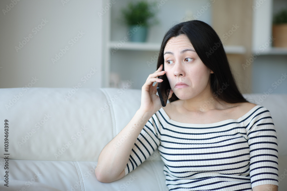 Perplexed asian woman talking on phone at home Perplexed asian woman talking on phone at home