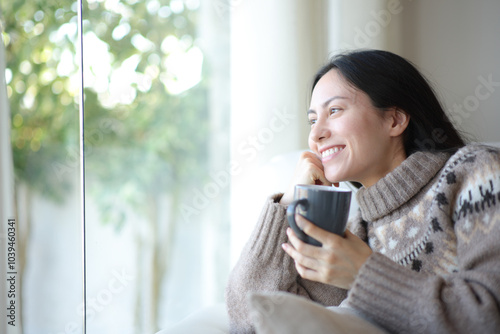 Asian woman drinking coffee in winter looking through a wiindow