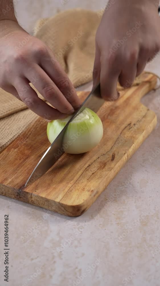 Vertical Screen: Close-up of hands cutting an onion on a wooden board in two halves. Concept of chopping vegetables for cooking Vertical Screen: Close-up of hands cutting an onion on a wooden board in two halves. Concept of chopping vegetables for cooking
