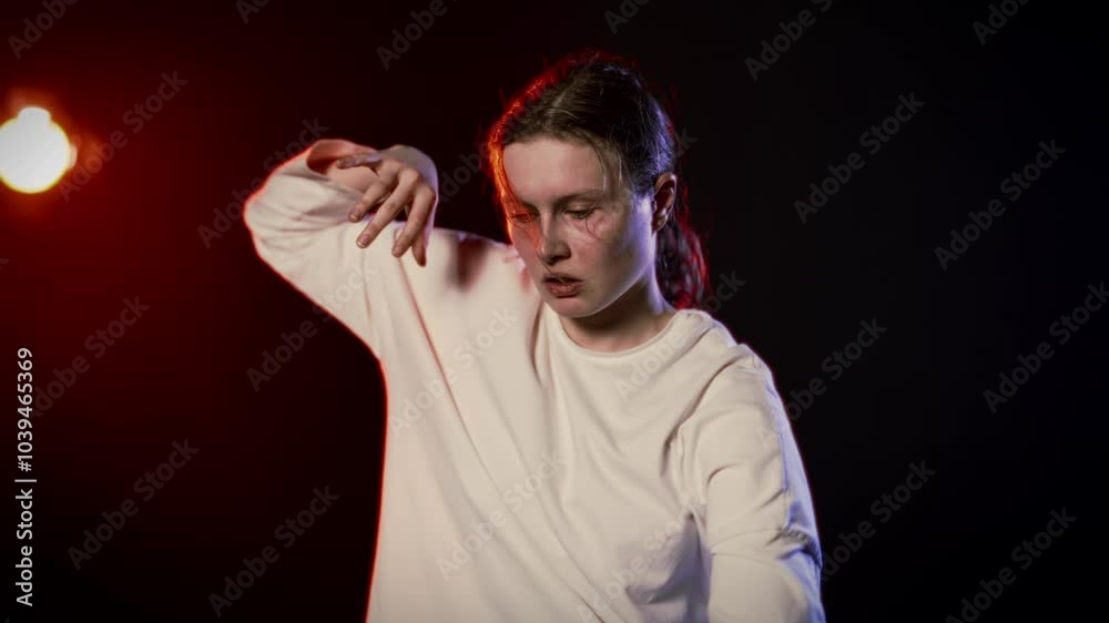 Madness and art, young crazy woman dancing alone in studio, looking at camera. Strange face expression and movements, cinematic medium portrait in darkness, red and blue soffits in black background Madness and art, young crazy woman dancing alone in studio, looking at camera. Strange face expression and movements, cinematic medium portrait in darkness, red and blue soffits in black background