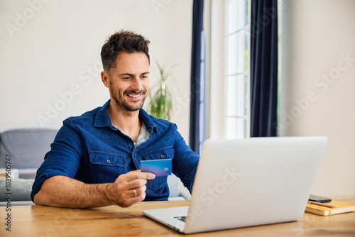 Happy man shopping online with credit card at home using laptop photo