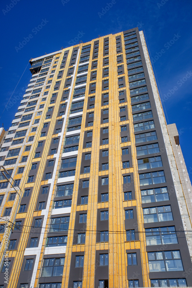 A tall building with a yellow facade and a blue sky in the background A tall building with a yellow facade and a blue sky in the background