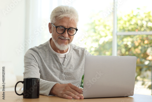 Senior man using laptop at table indoors