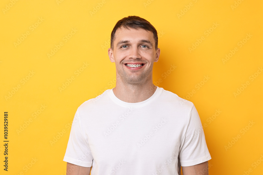 Smiling man with dental braces on yellow background Smiling man with dental braces on yellow background