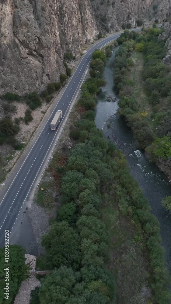 Vertical drone shot along a scenic road between rocky hills and green trees Vertical drone shot along a scenic road between rocky hills and green trees